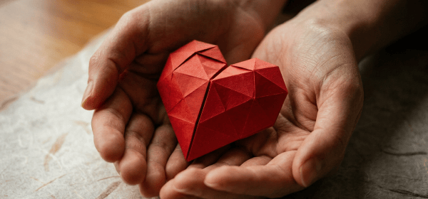 Red origami heart held in two cupped paper hands
