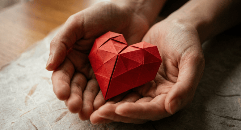 Red origami heart held in two cupped paper hands